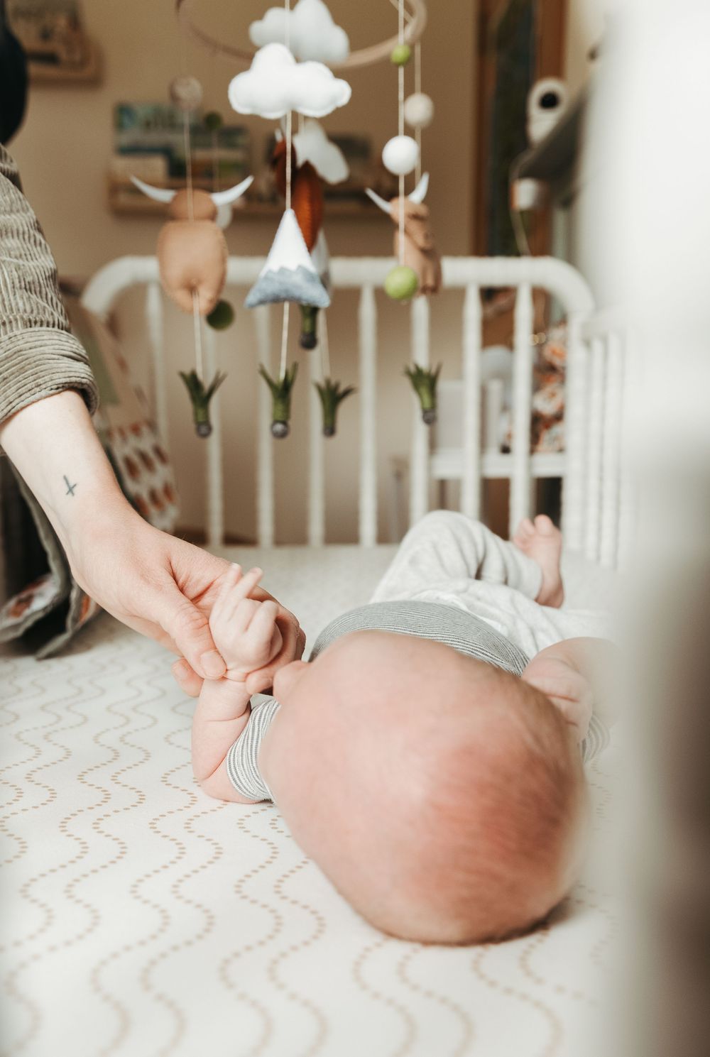 A baby lies on a white patterned crib mattress under a cloud mobile hanging from above.