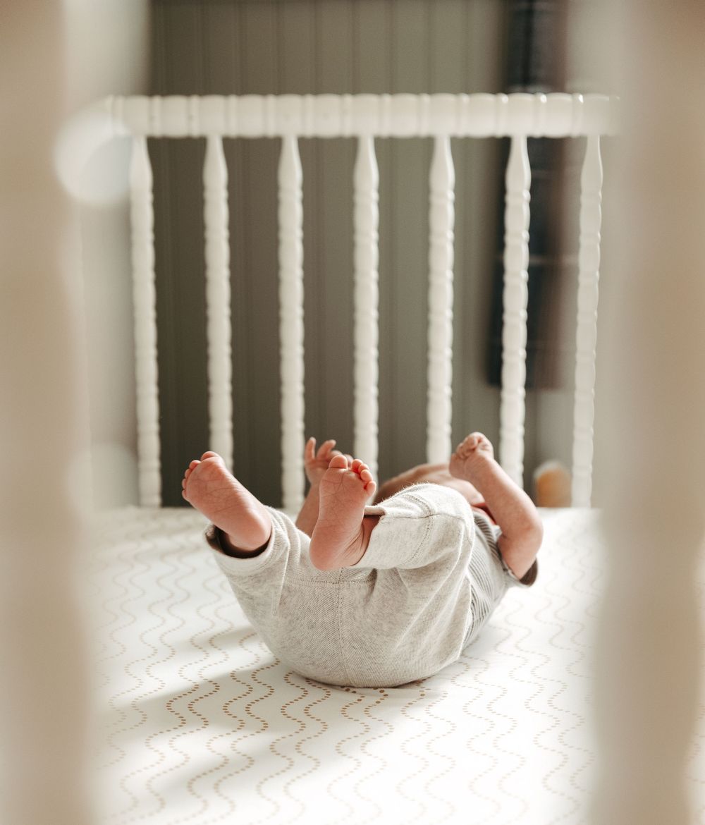 Tiny baby feet peek through white crib slats against a soft, blurred background.