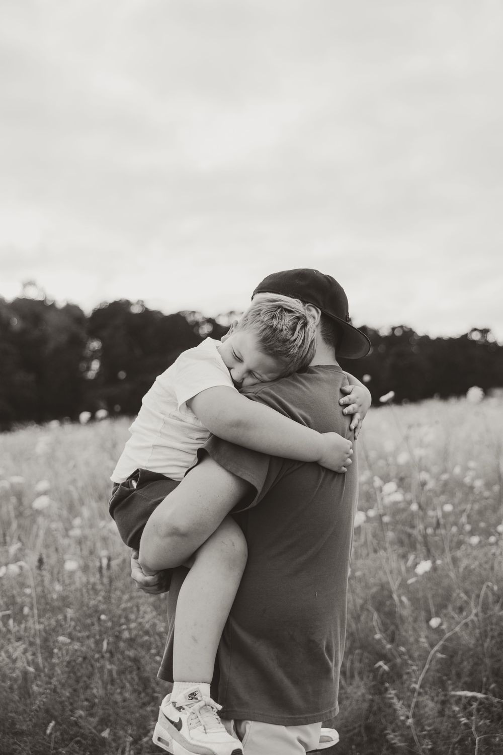 Black and white photo of a child being held and hugging an adult in a wildflower field.
