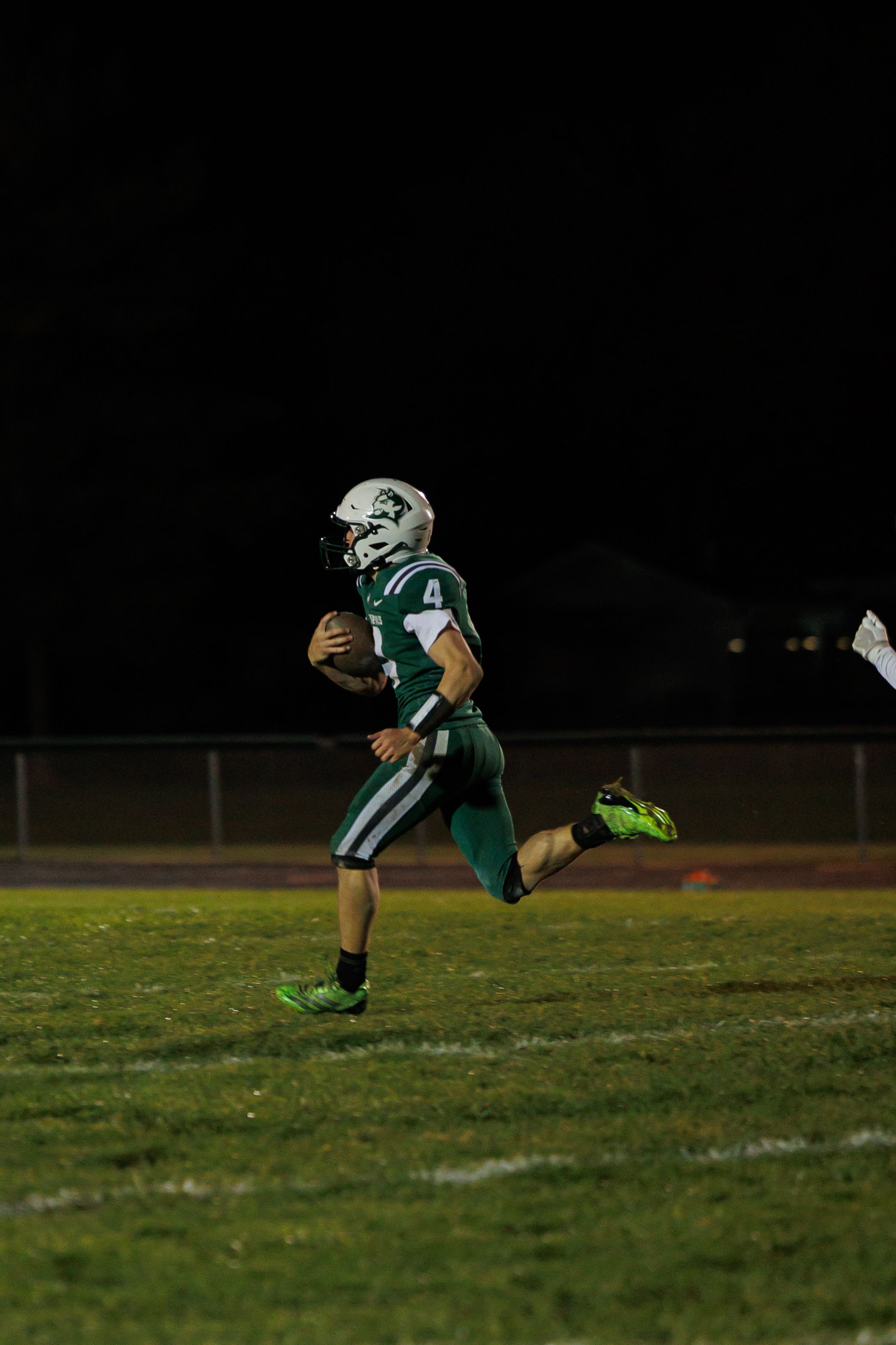 Football player in green jersey runs across field during nighttime game under stadium lights.
