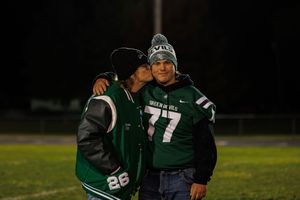 Football players huddle together on a dark field during nighttime practice wearing green and white uniforms.