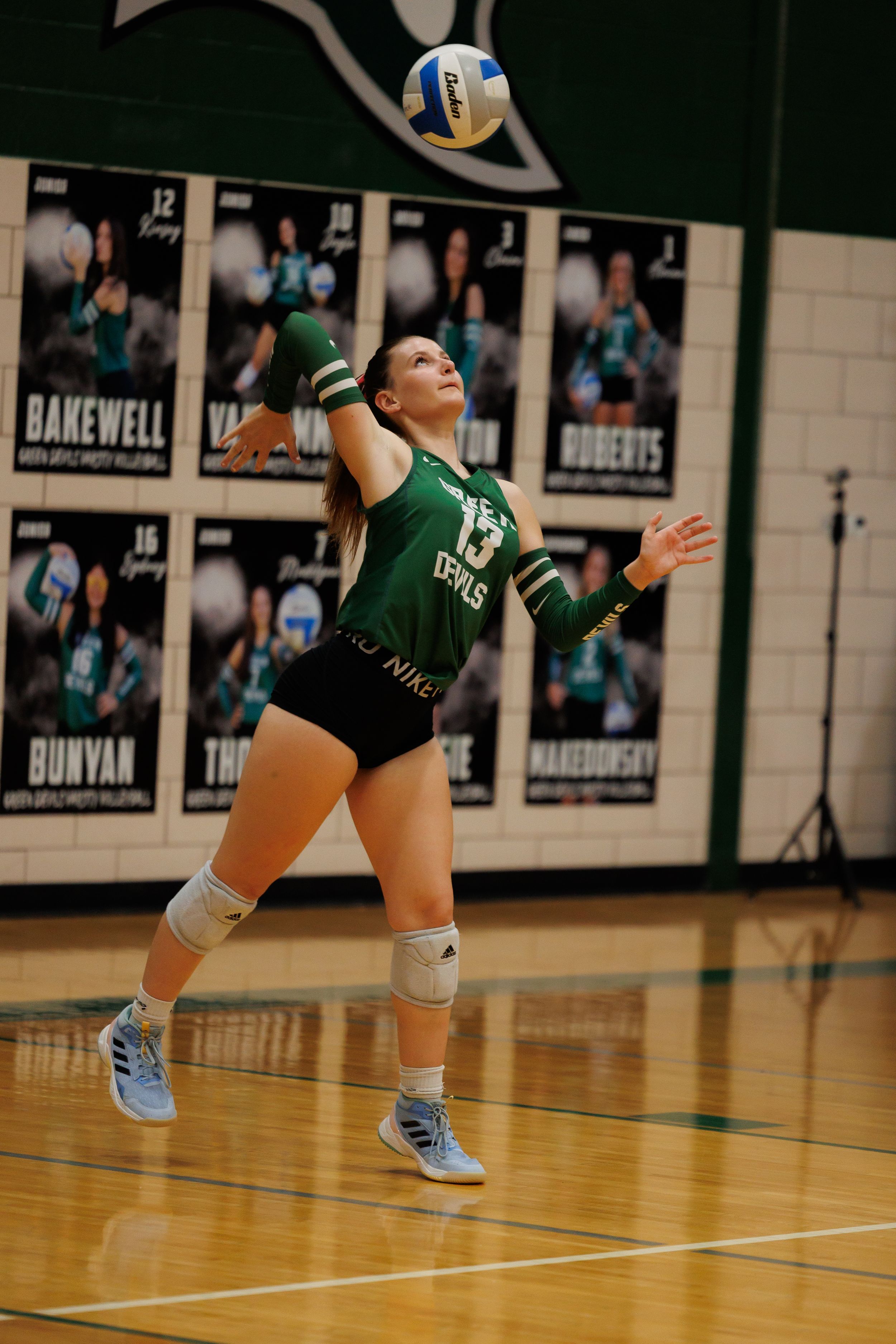 Volleyball player in green uniform dives to save the ball during an indoor match on a polished wooden court.