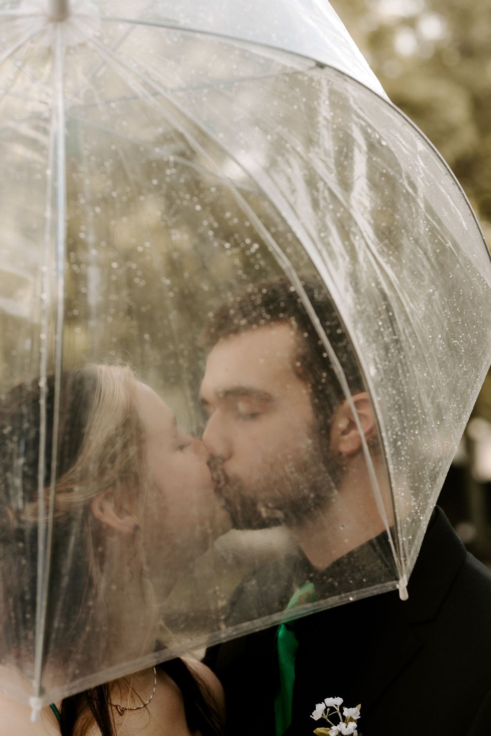 A couple shares a romantic kiss under a clear umbrella in the rain.
