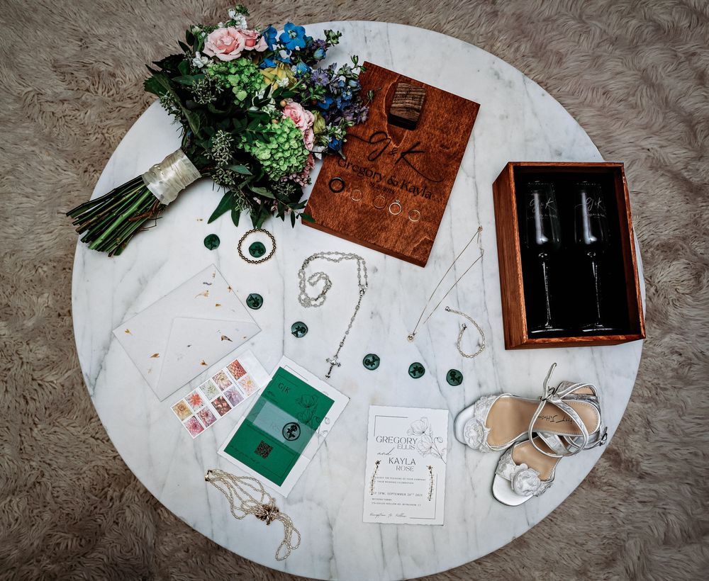 Wedding details and stationery arranged on a white surface with blue and pink flowers and rustic decorative elements.