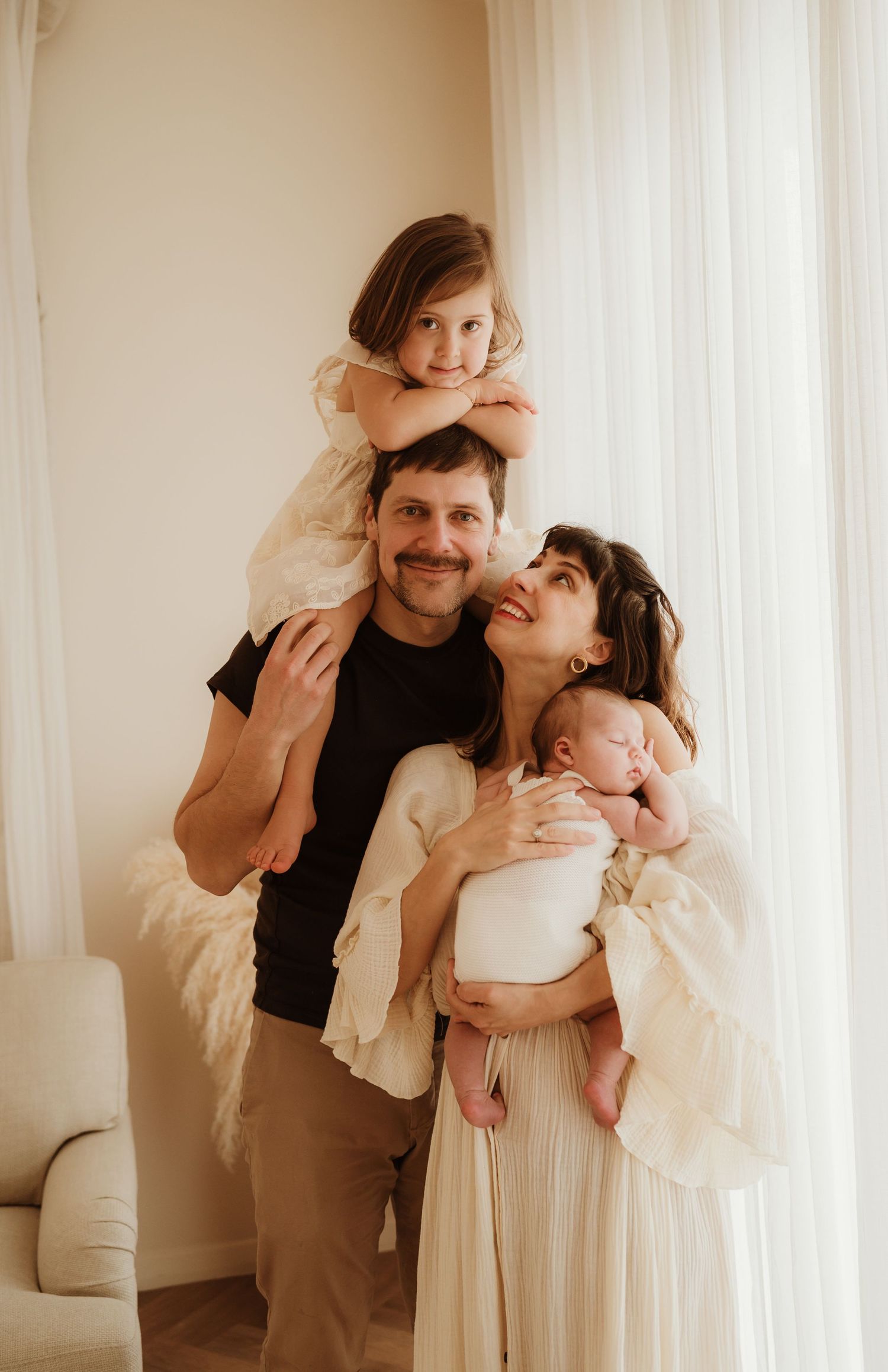 A warm family portrait in muted beige tones shows parents with their two children against a light curtained background.