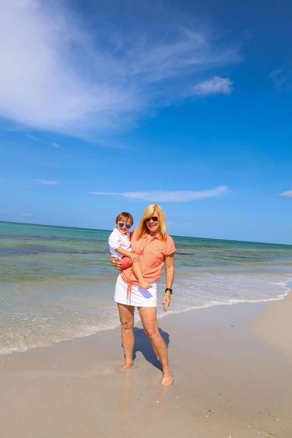 Two people enjoying a sunny day at the beach with turquoise water and white sand under bright blue skies.