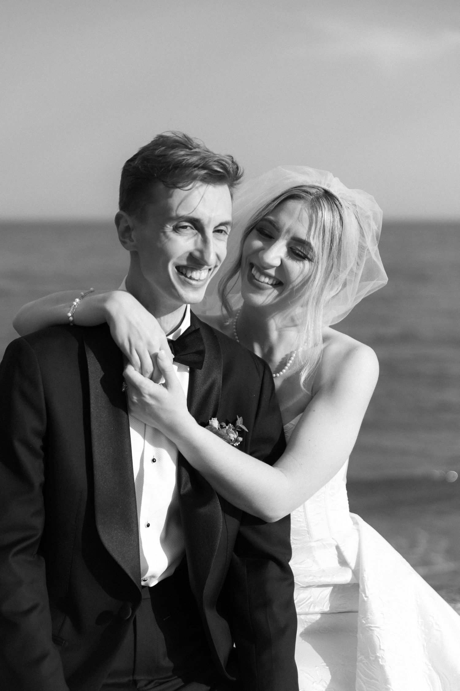 A joyful wedding couple shares intimate moments in black and white photos by the ocean.