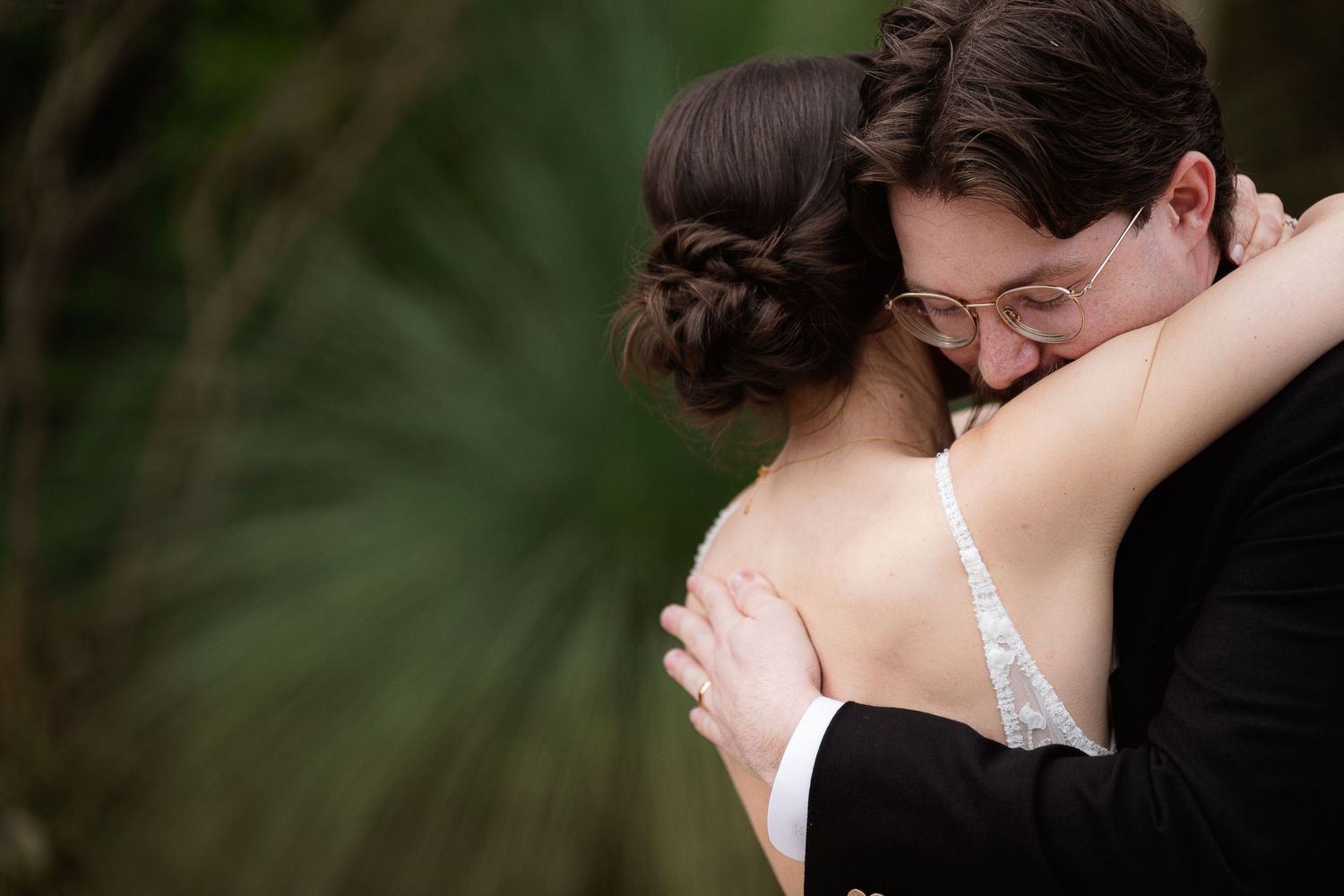 A romantic moment captured between newlyweds embracing in a garden surrounded by lush silver-green foliage on their wedding day.