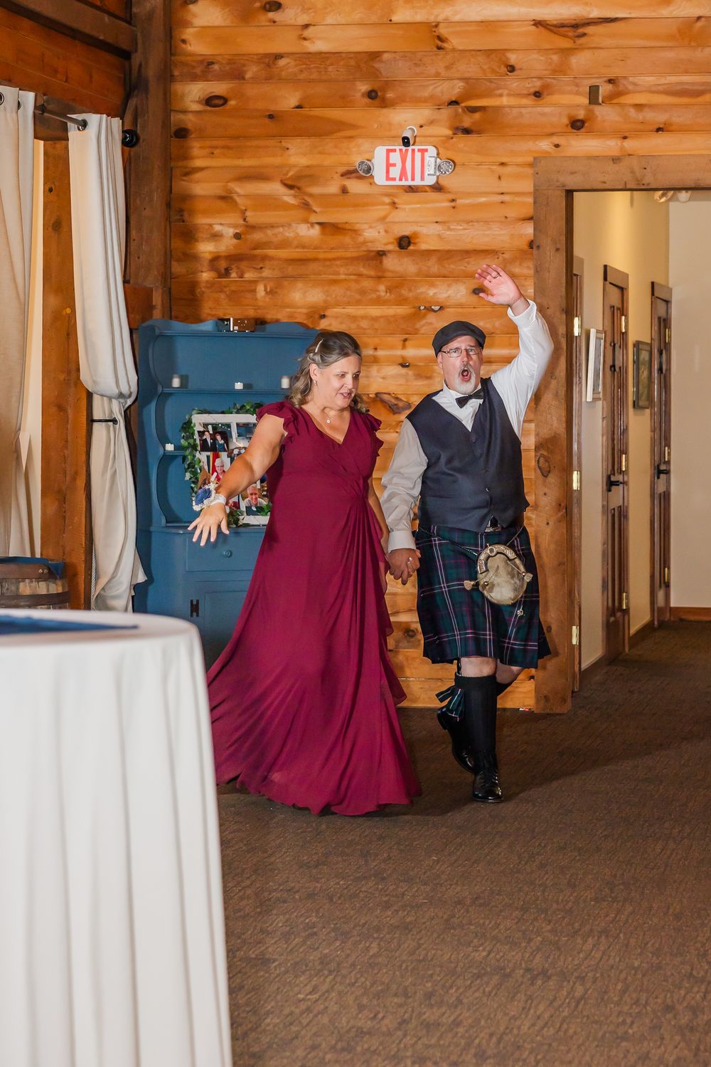 Wedding party dancing and celebrating in a rustic wood-paneled venue with white drapes and warm lighting.