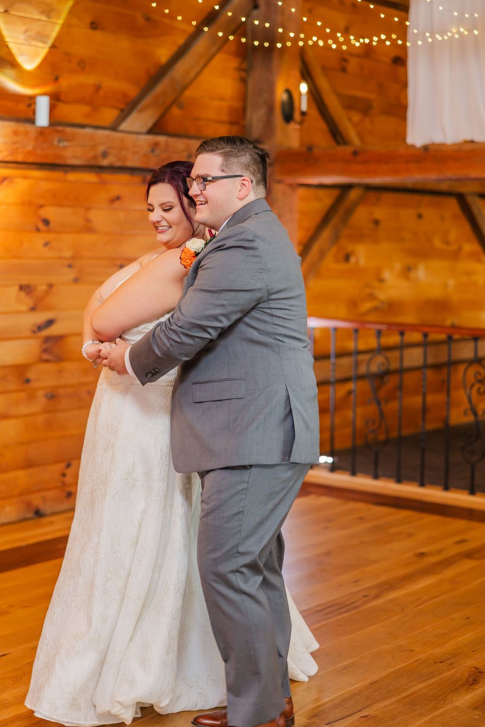 A couple shares their first dance in a rustic wooden barn venue decorated with twinkling string lights.