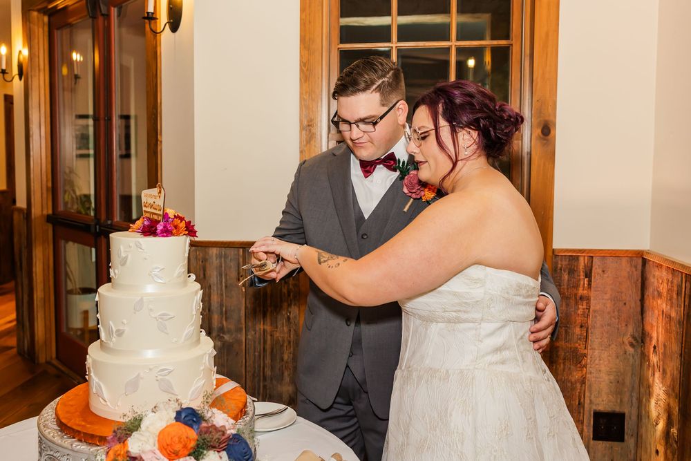 A wedding couple shares a sweet moment while cutting their white tiered wedding cake at the reception.