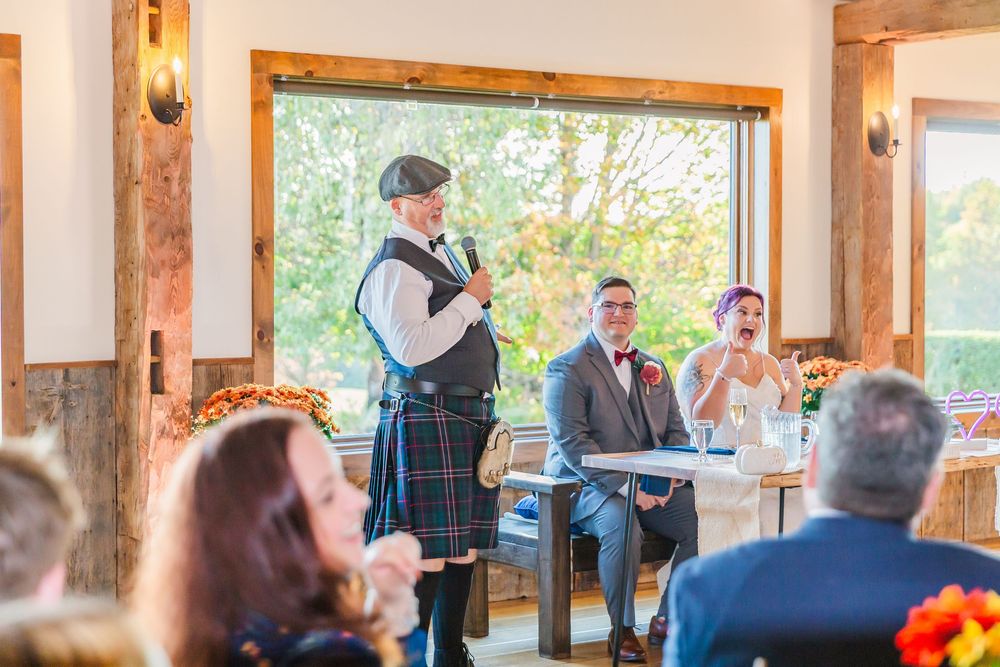 Wedding guests enjoy an indoor reception at a rustic venue with exposed wooden beams and natural lighting.