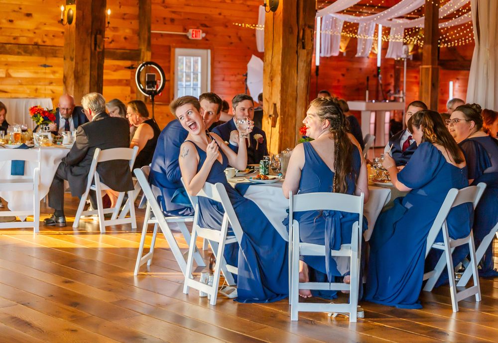 Wedding guests in navy blue attire seated in white chairs during an indoor rustic barn ceremony.