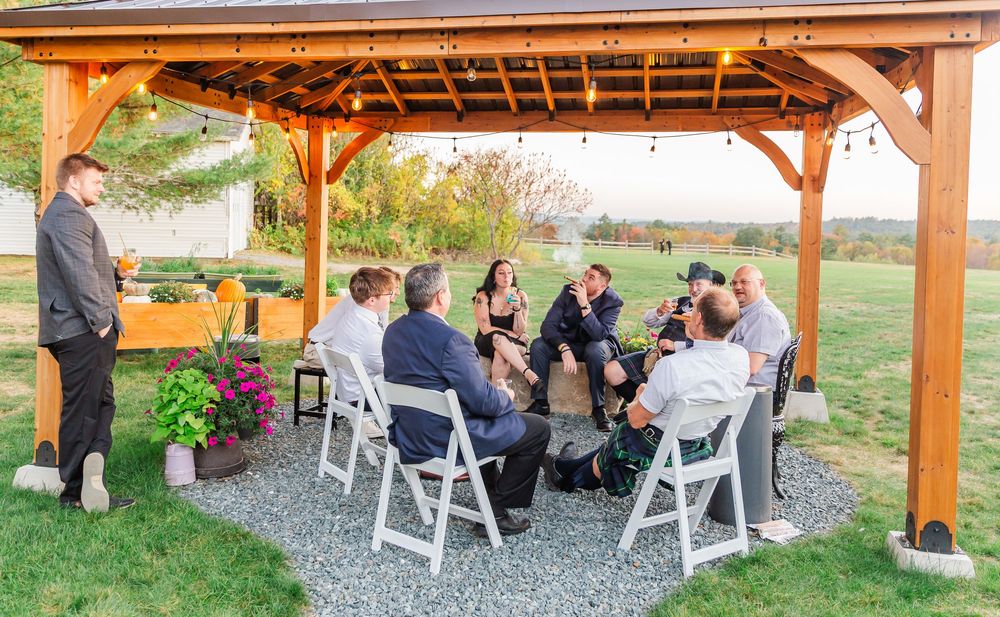 Panoramic view of an outdoor covered patio with white chairs and guests gathered under a wooden pergola structure.