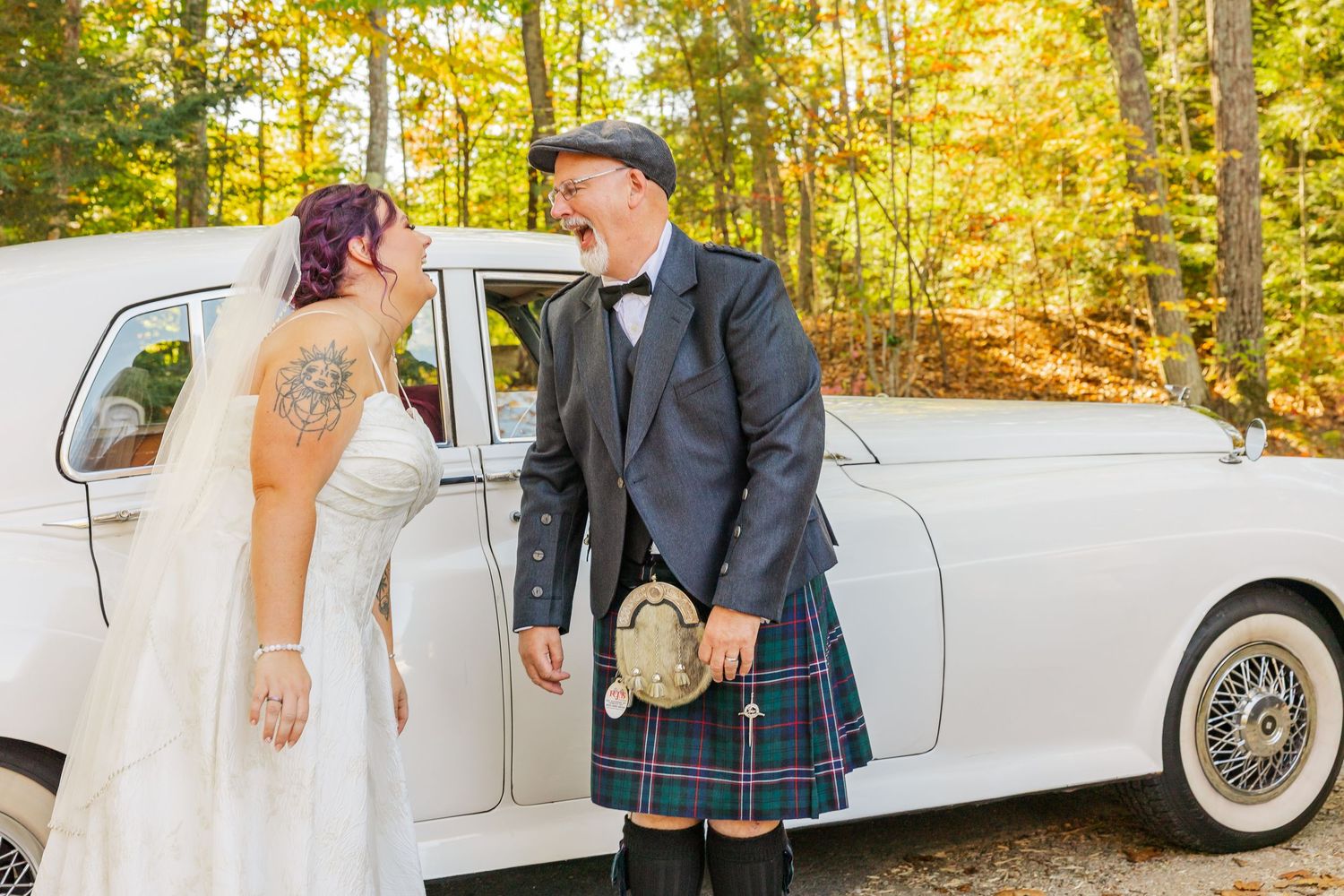 Wedding party poses with vintage white car in autumn forest setting with golden sunlight.