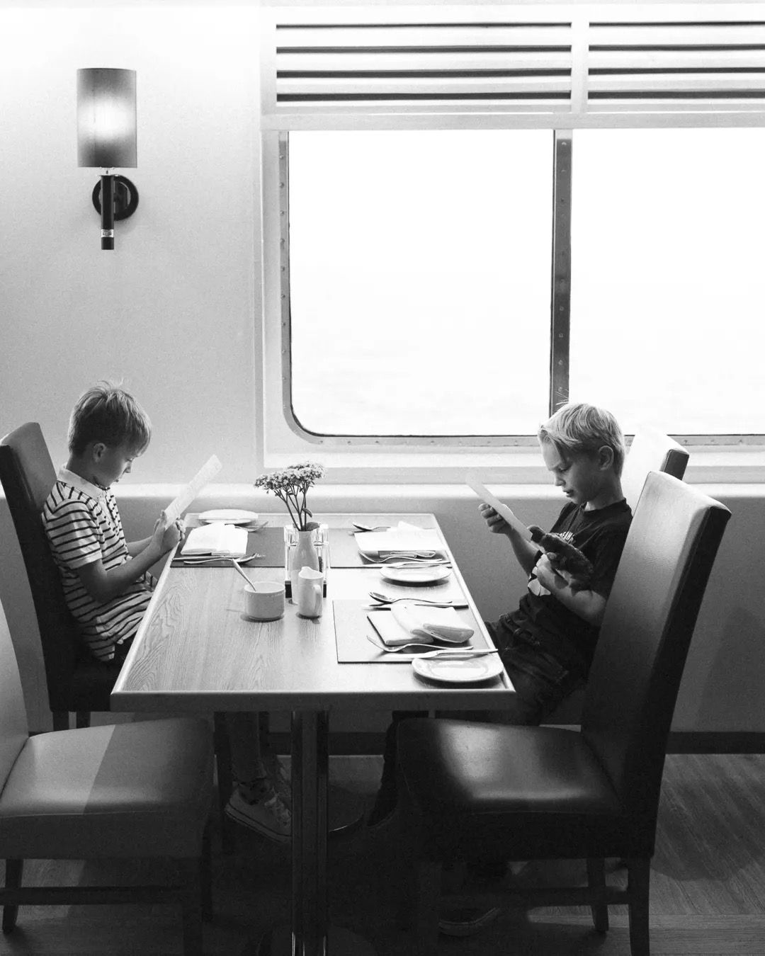 Two children having a meal at a small table on a train in black and white.