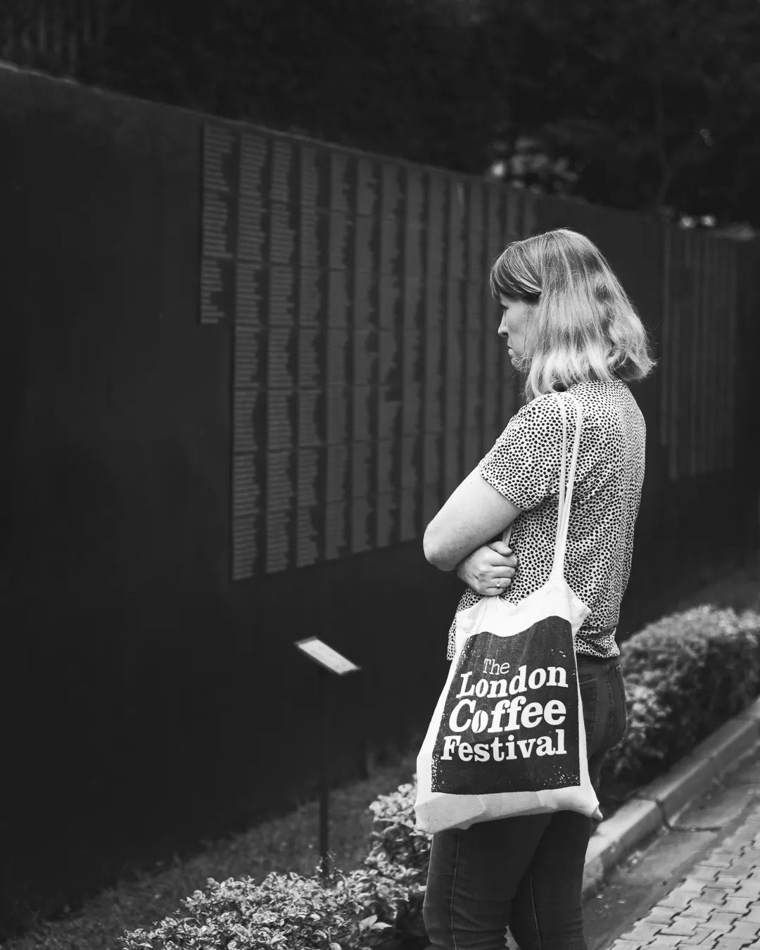 Woman carries a bag while walking outdoors in a candid black and white moment.