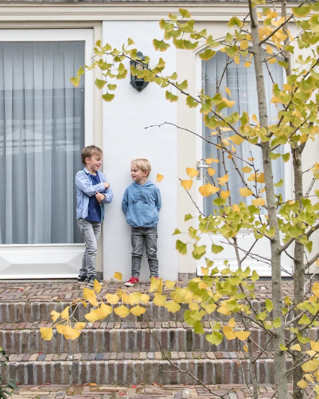 Family standing on a front step beside an autumn tree with golden leaves, soft natural light.