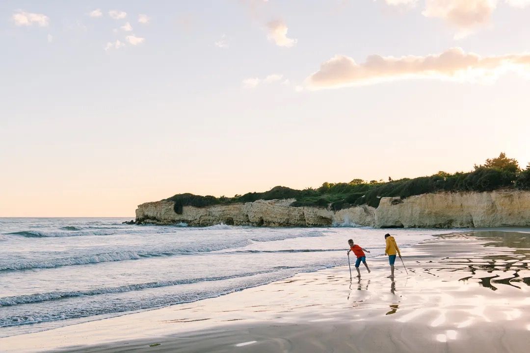 Two children play at the water’s edge during sunset, enjoying the beach and gentle waves.