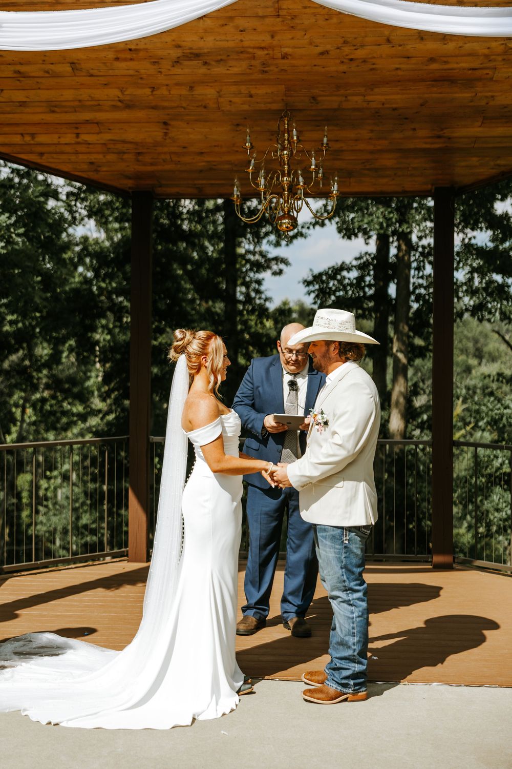 A romantic first look moment unfolds between a couple on a rustic wooden deck surrounded by trees.