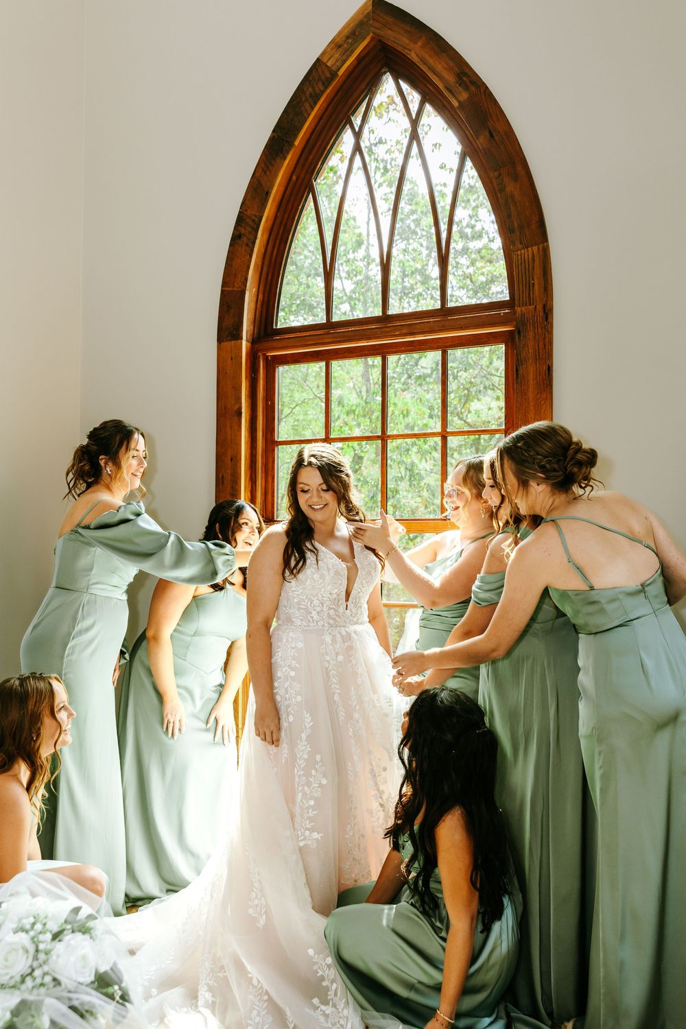 A sequence of candid wedding moments showing bridesmaids in sage green dresses helping with the bride's gown near arched windows. WV Wedding