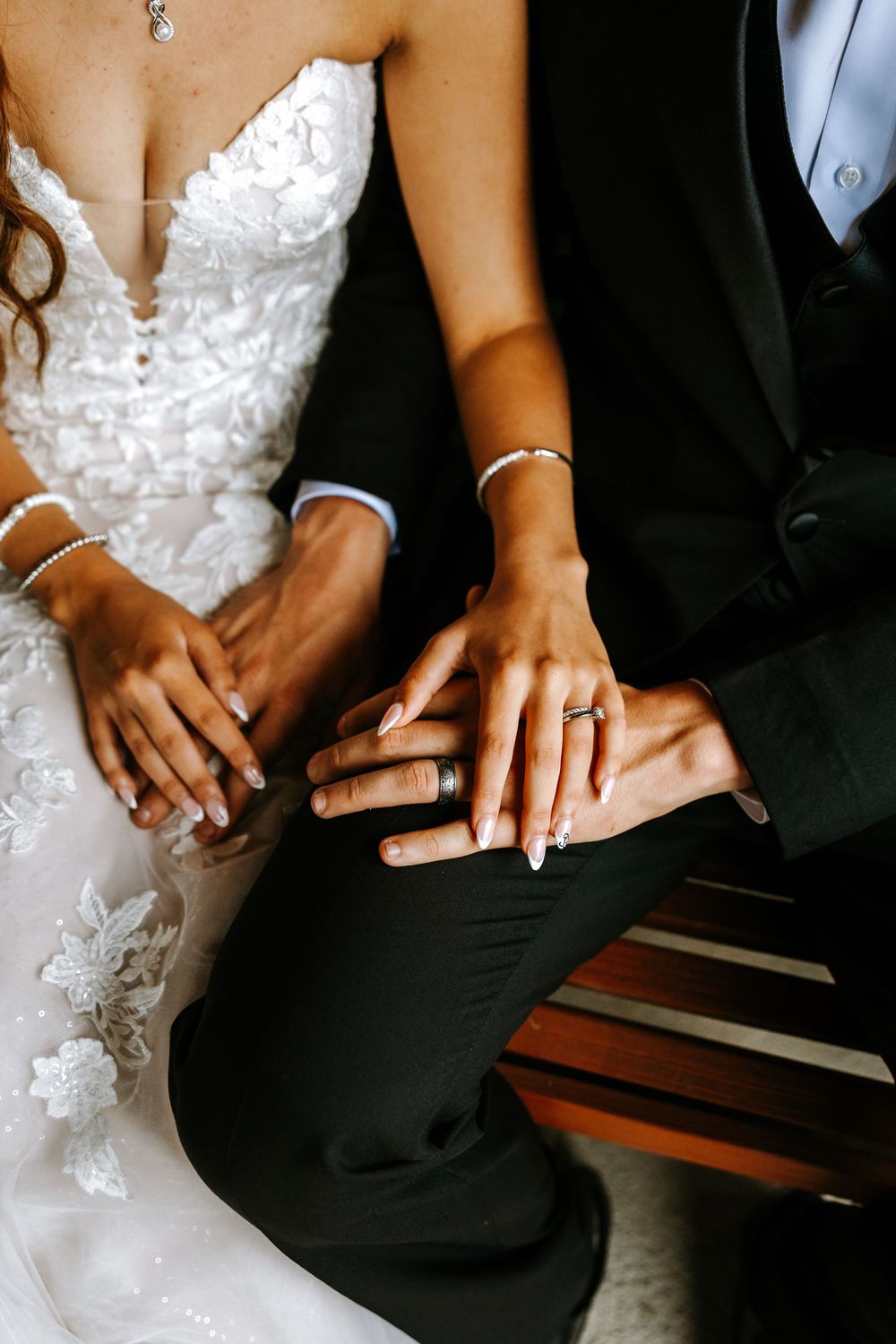 Close-up of newlywed couples' hands showing wedding rings and white bridal gowns against black suits.
