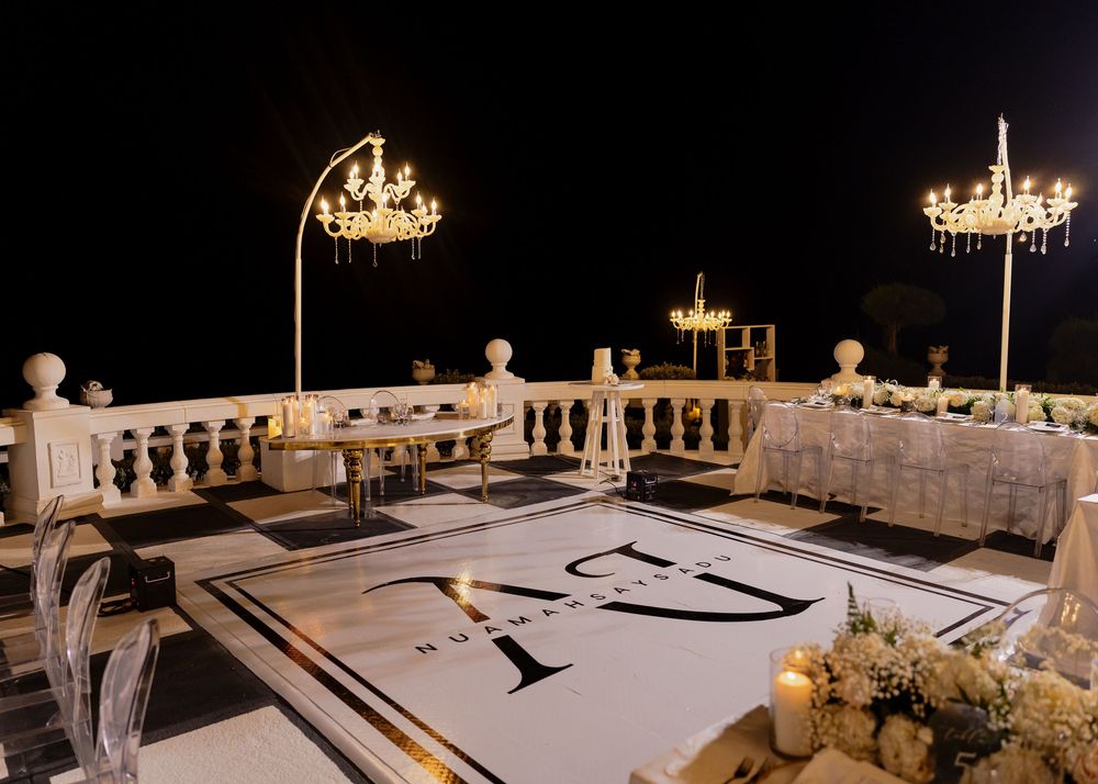 Elegant wedding reception setup with white tables, crystal chandeliers and floral arrangements in a dimly lit ballroom.