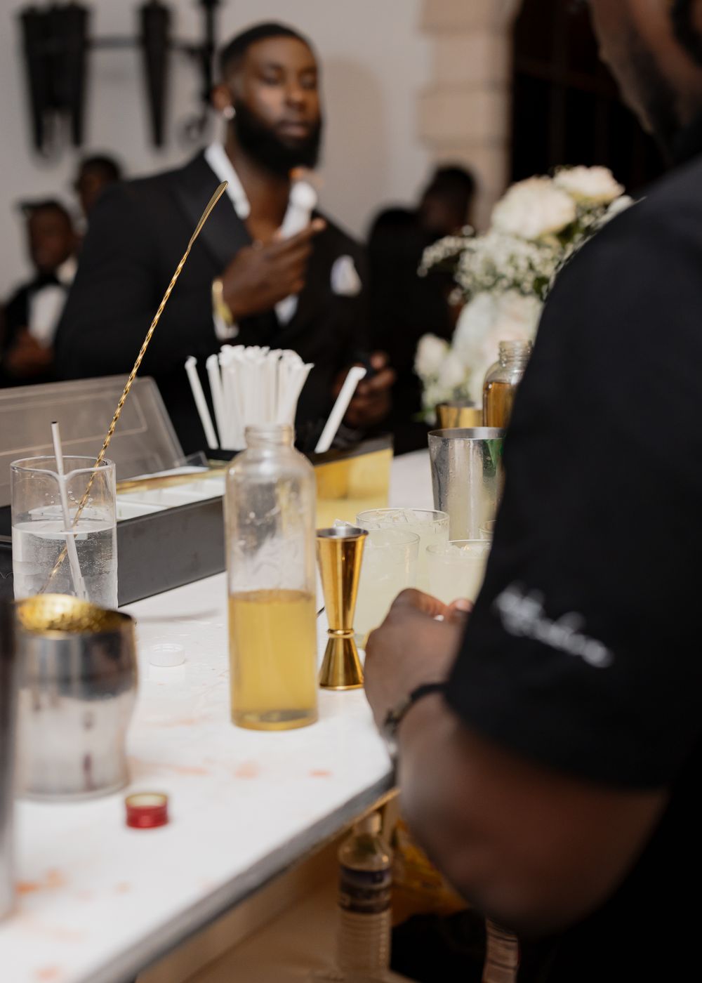Guests at an elegant bar setting with drinks and glassware arranged on a white countertop.