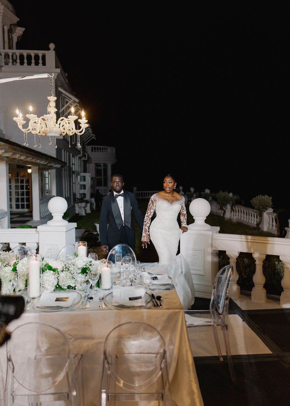 Elegant wedding reception setup with white table linens, floral centerpieces and crystal chandeliers in a grand venue.