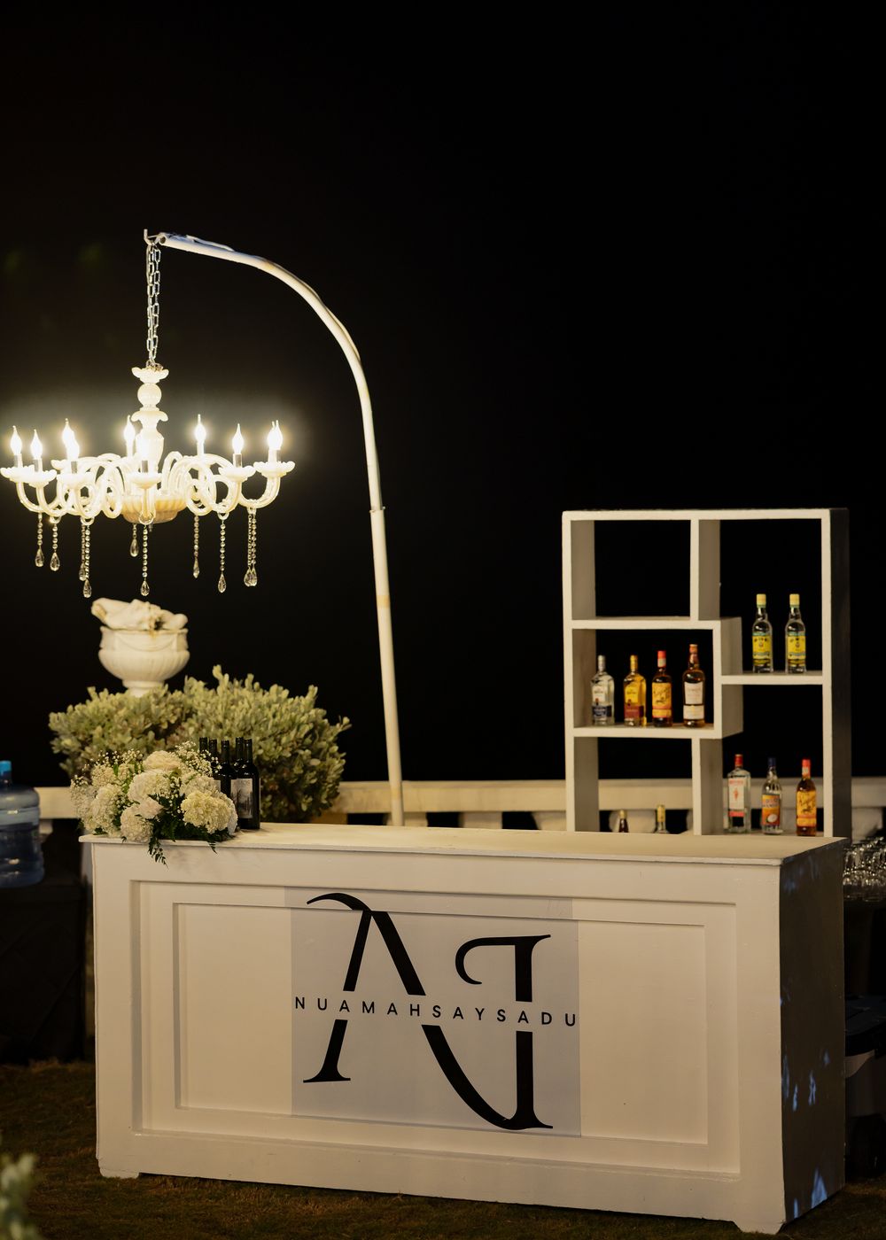 Elegant white bar setup with illuminated chandeliers and bottle displays creating an upscale ambiance.