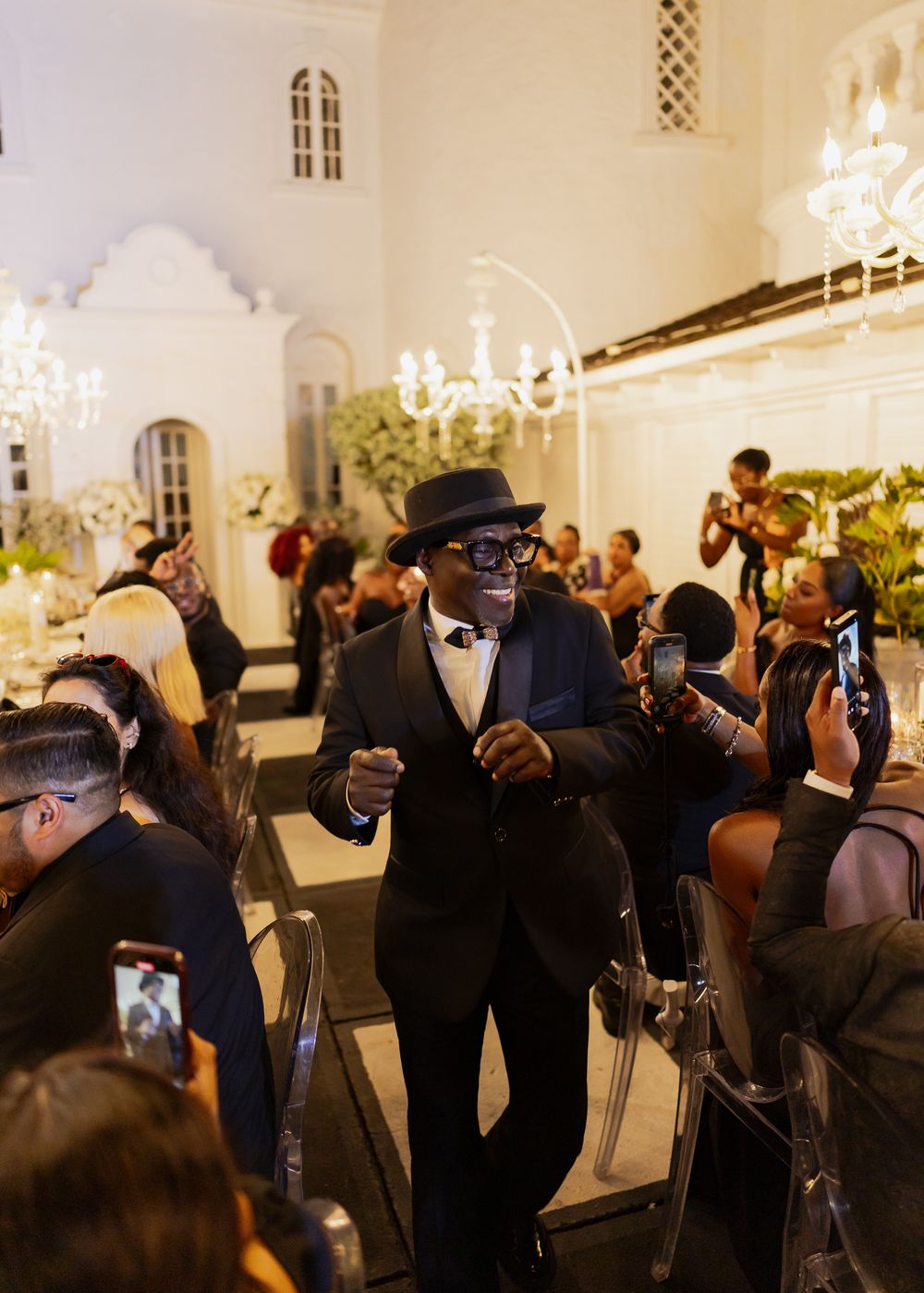 A group of photographers with cameras gather in an elegant room with chandeliers to capture an event.