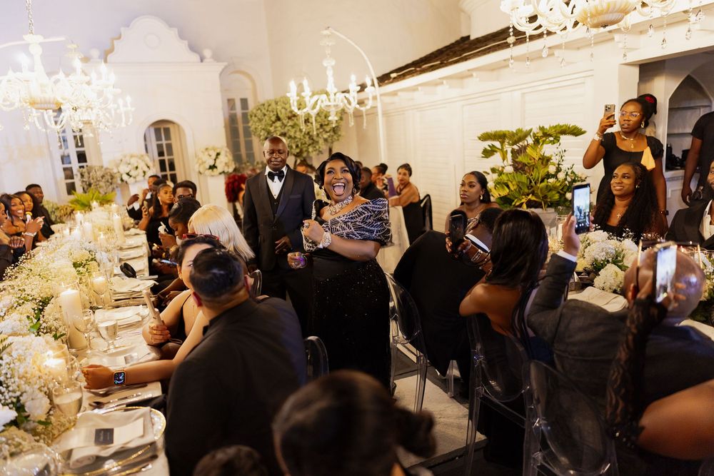 Wedding guests mingle and socialize during an elegant indoor reception with chandeliers and floral arrangements.