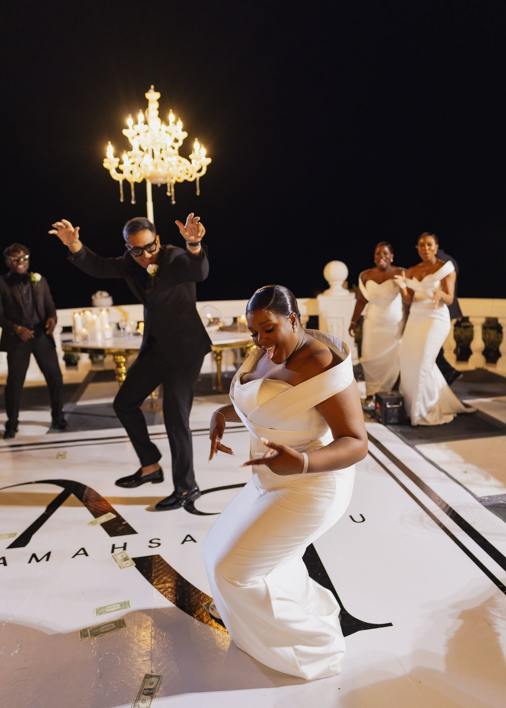 Wedding party dancing and celebrating on an elegant white dance floor with black lettering under a crystal chandelier.