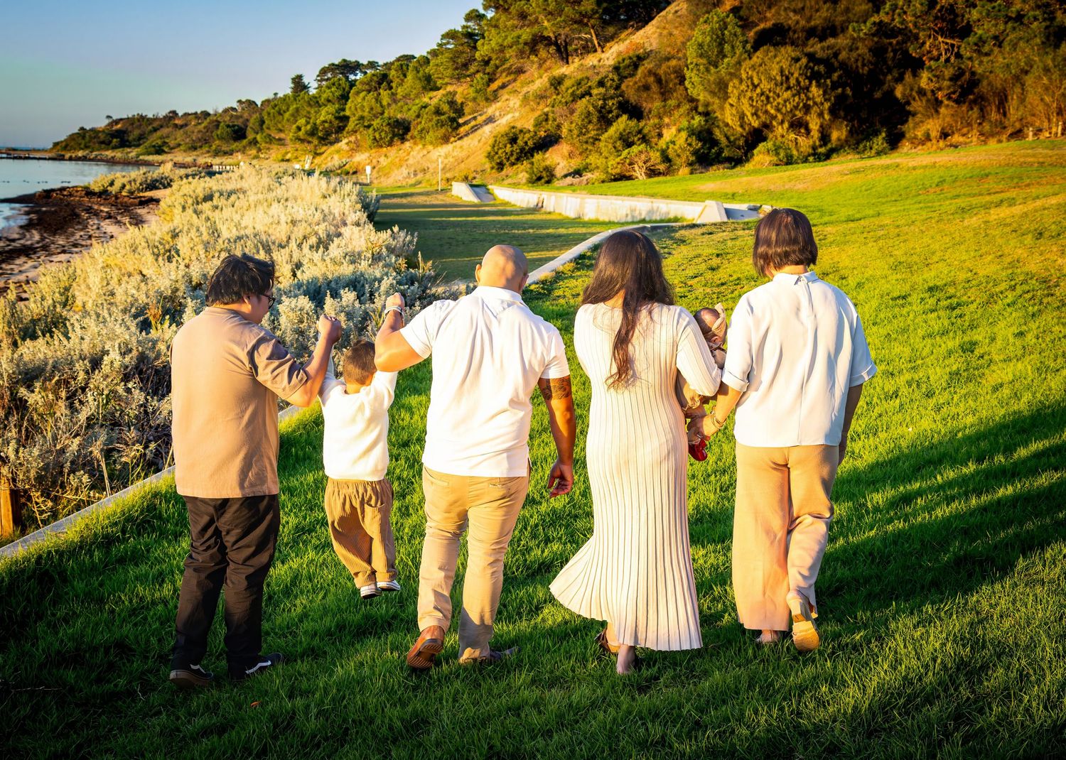 Wedding party poses on grassy hillside overlooking coastal views at sunset.