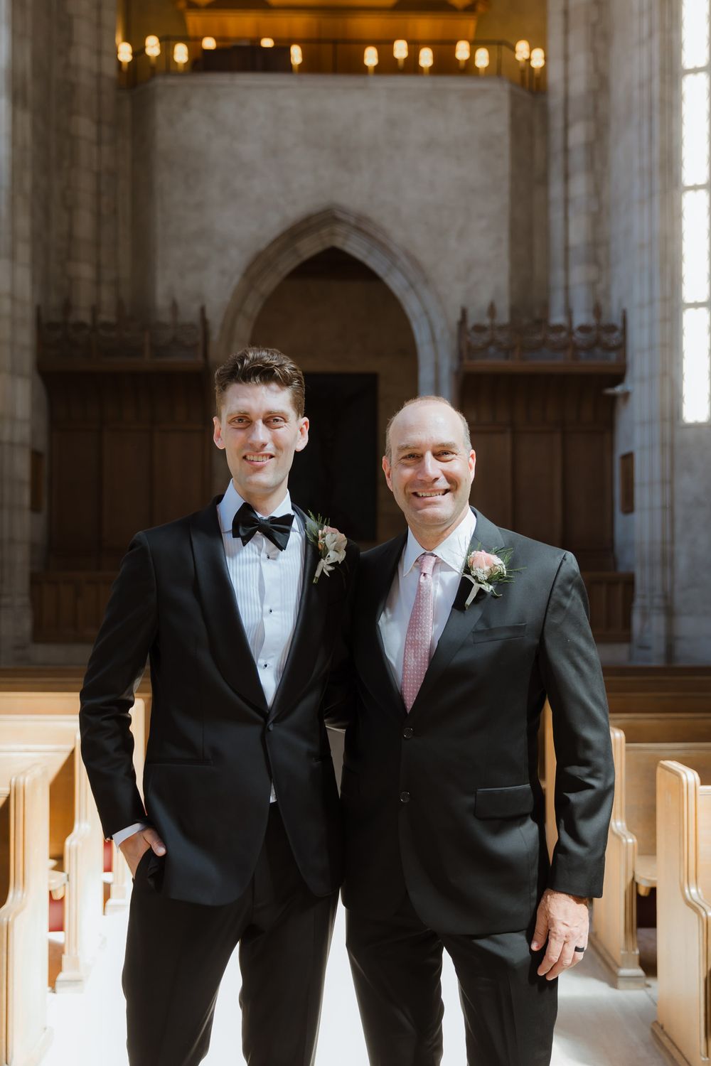 Two people in formal attire stand together in church with gothic architecture.