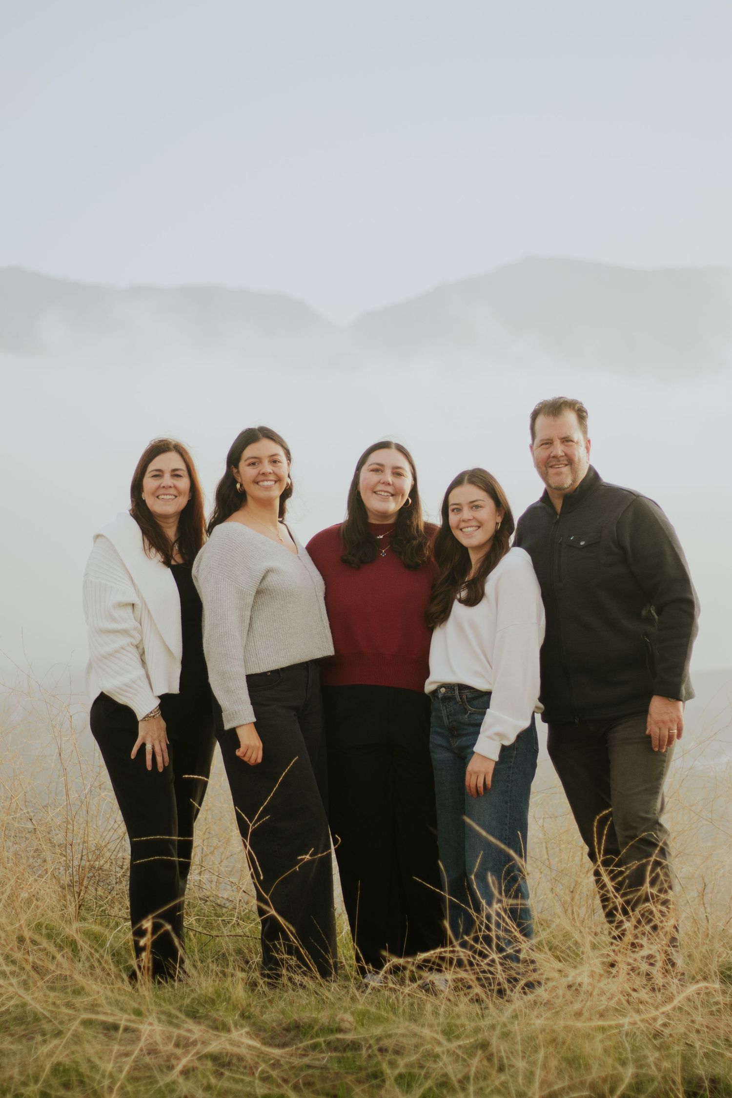 A group stands together in casual attire against a misty outdoor backdrop with tall grass.