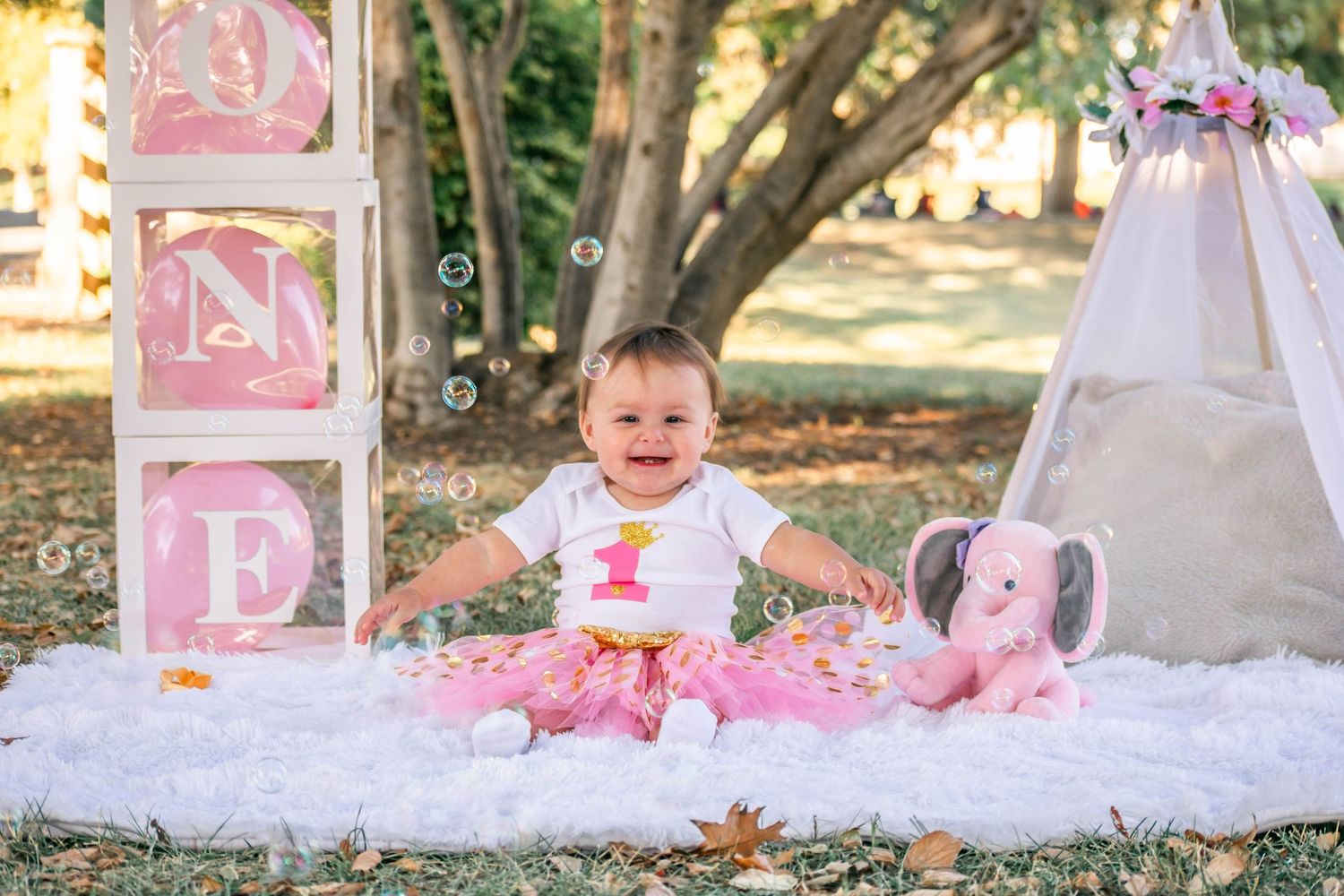 Pink and white decorative blocks and party accessories arranged outdoors for a first birthday celebration photoshoot.
