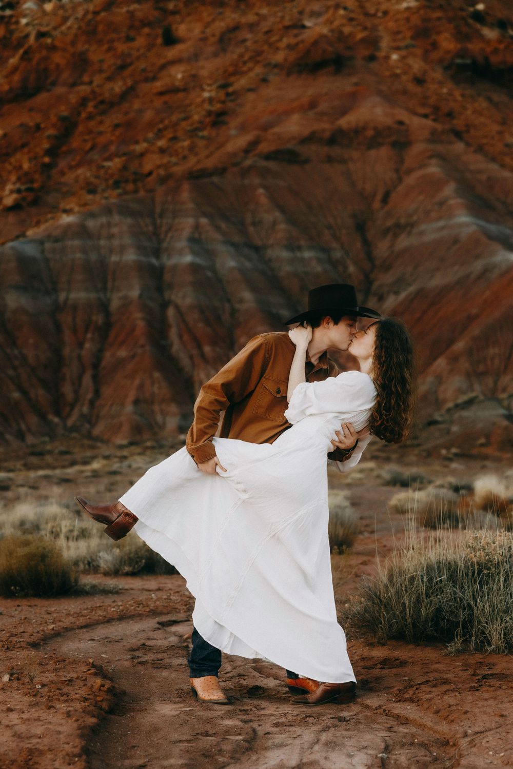 Couple sharing romantic dip kiss in front of red rock canyon desert landscape.