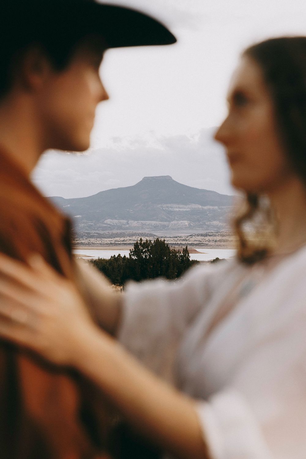 Blurred couple facing each other with scenic mountain and lake vista between them.