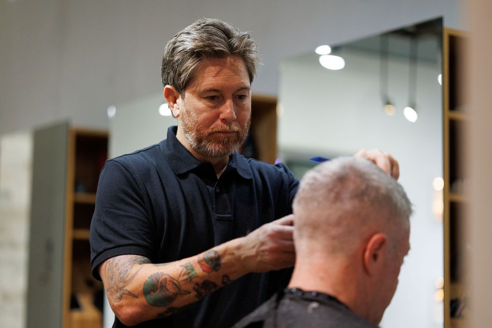 Hairstylist with sleeve tattoos working on client's hair in modern salon.
