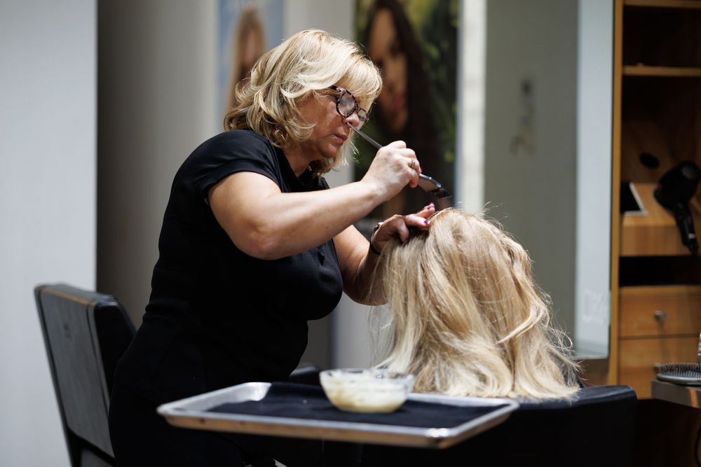 Stylist in black attire working on client's hair at salon station.