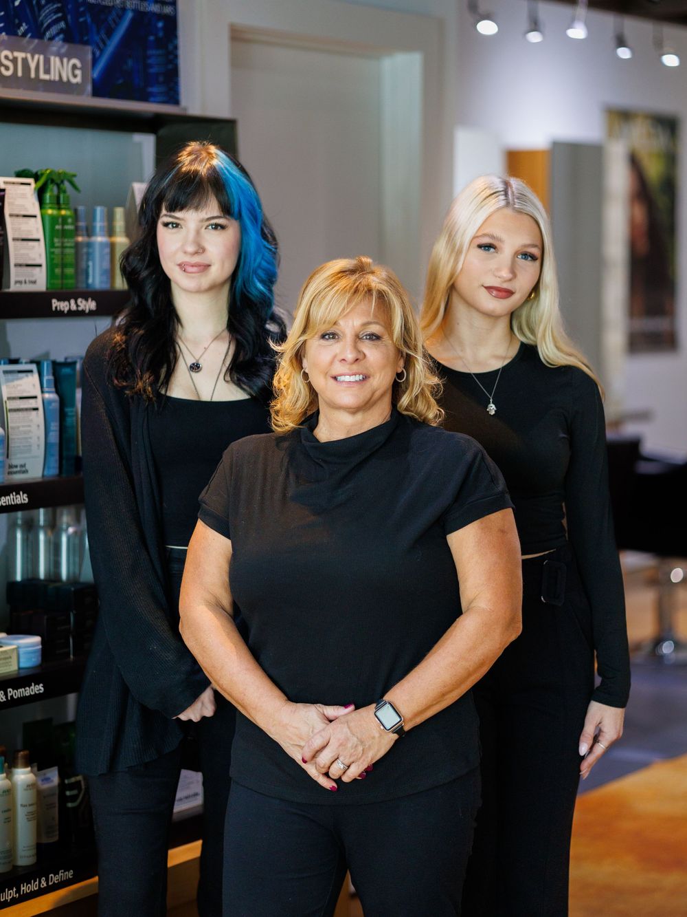 Salon staff members pose together in black attire inside their modern beauty store.