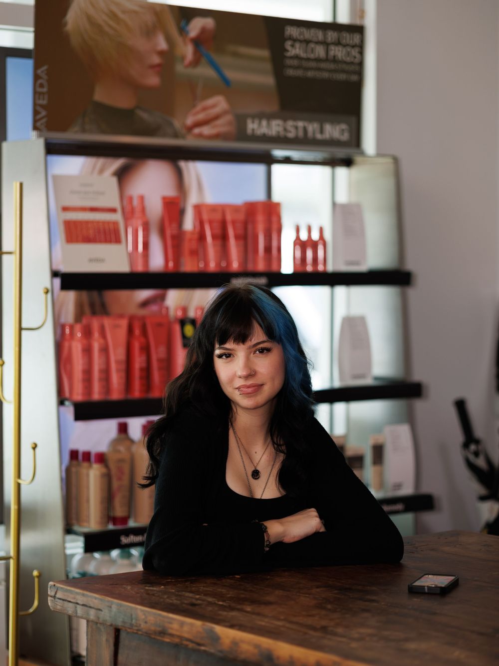 Professional salon interior with dark wood desk and styling products displayed on shelves.
