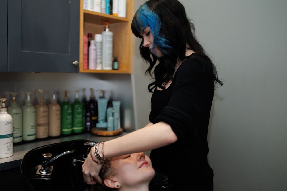 Stylist working in modern salon with product shelves visible in background.