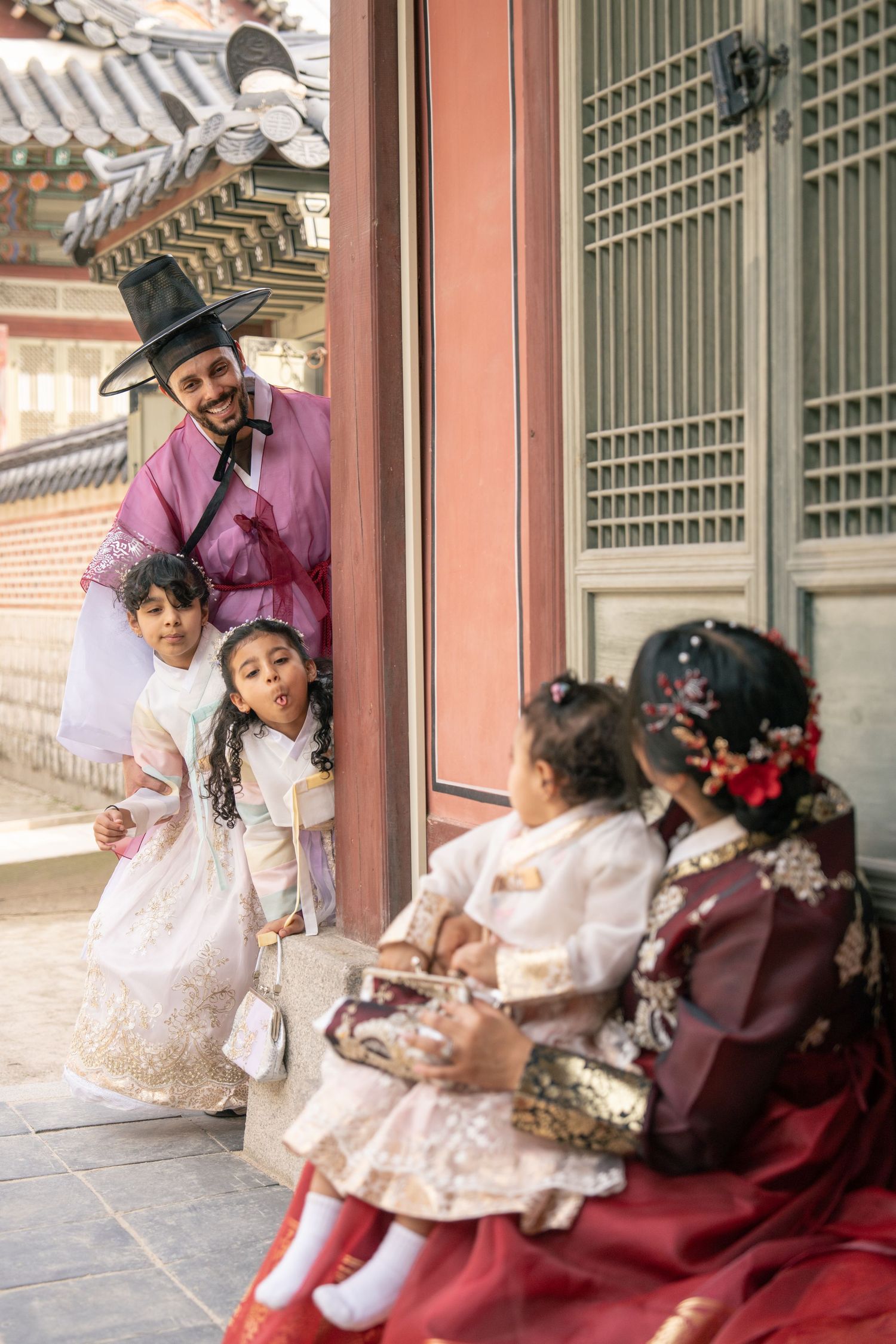 People in traditional Korean hanbok clothing sit together on a wooden porch of a historic building.