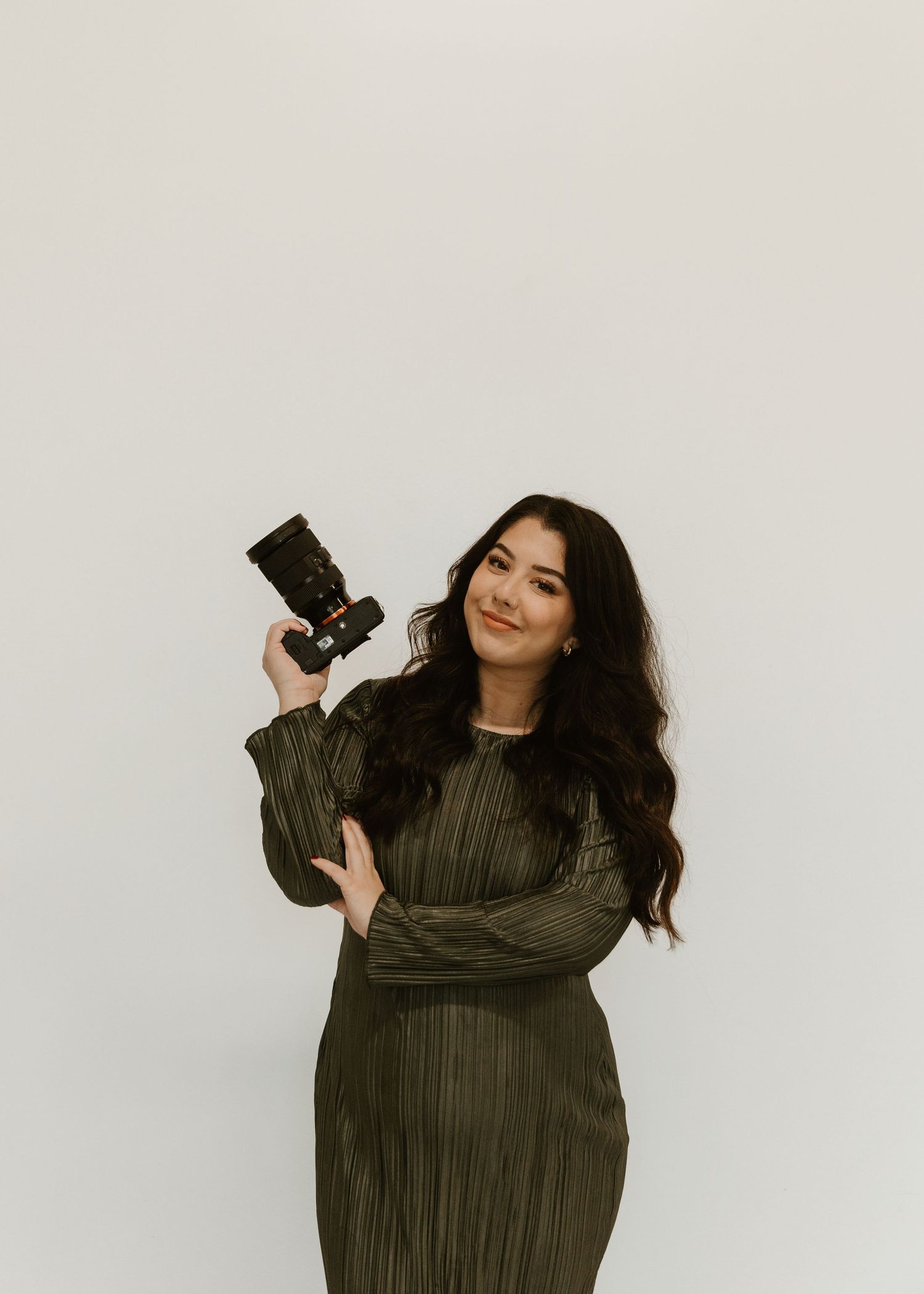 Woman in black top and white pants poses against gray paneled wall in modern indoor setting.