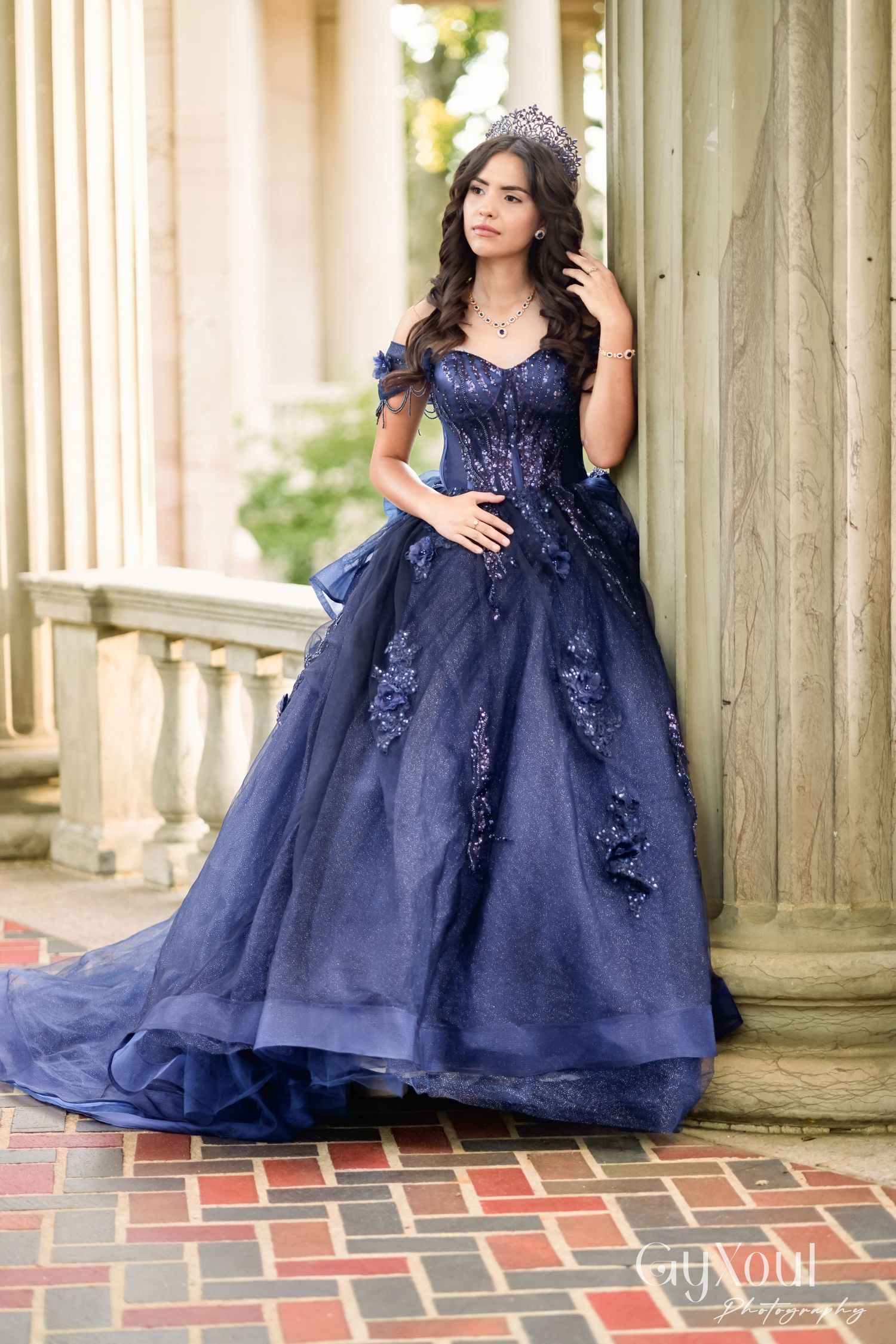 A stunning navy blue ball gown with lace appliques and off-shoulder design photographed against classical columns.