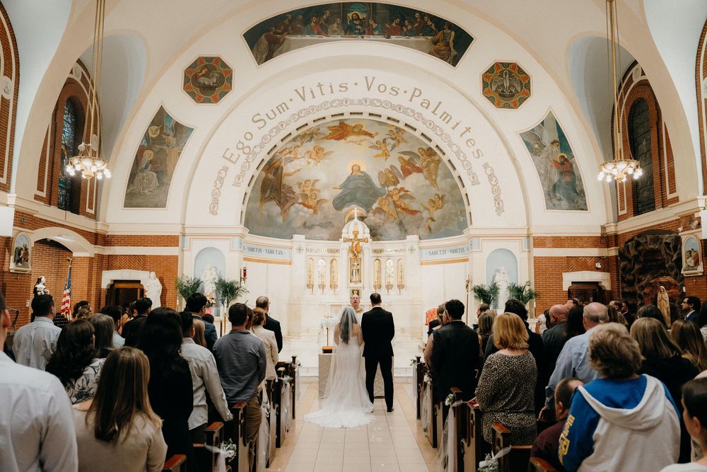 A wedding ceremony taking place in an ornate church with a painted dome ceiling and guests seated in wooden pews.