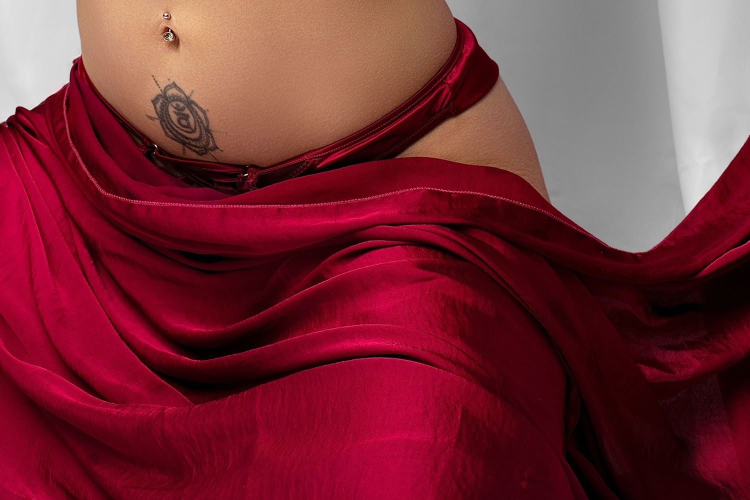 gorgeous mum of two burgundy lingerie poses elegantly with flowing red fabric against a light gray studio backdrop. classy bodiour.