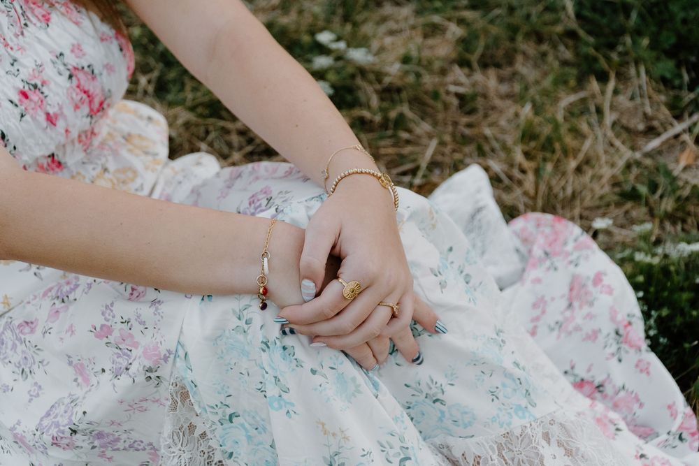 Hands gently unfold delicate white tulle fabric with pink floral patterns against a grassy outdoor background.